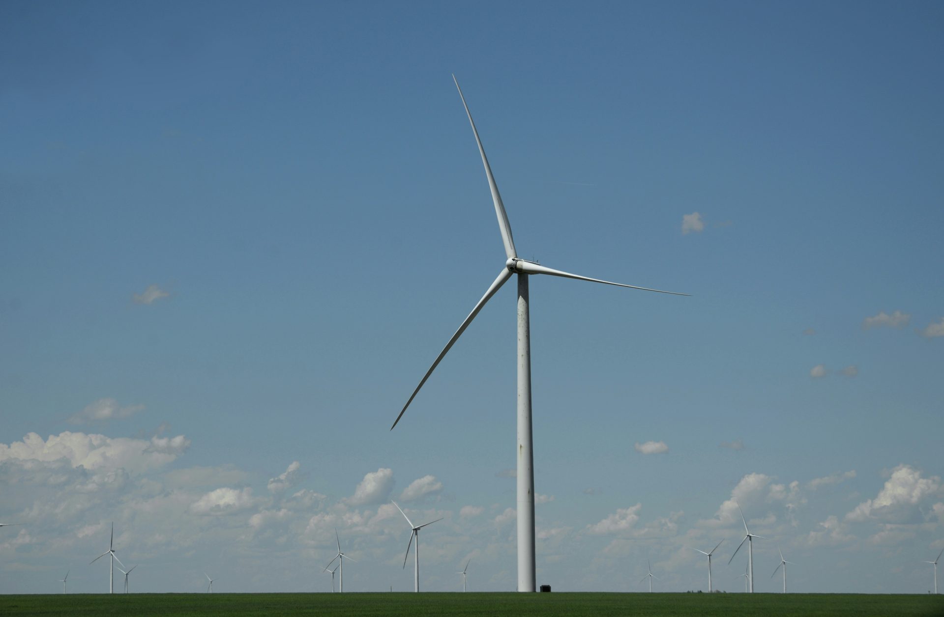 white wind turbine on green grass field under blue sky during daytime